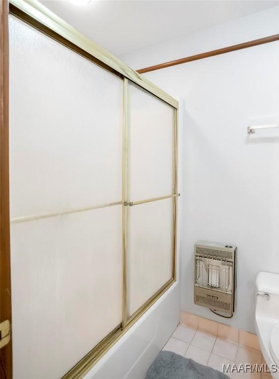 bathroom featuring heating unit, combined bath / shower with glass door, and toilet