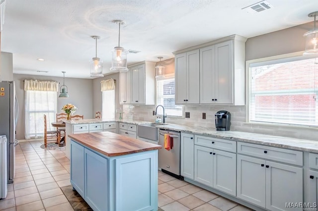 kitchen featuring a kitchen island, appliances with stainless steel finishes, decorative light fixtures, sink, and wooden counters