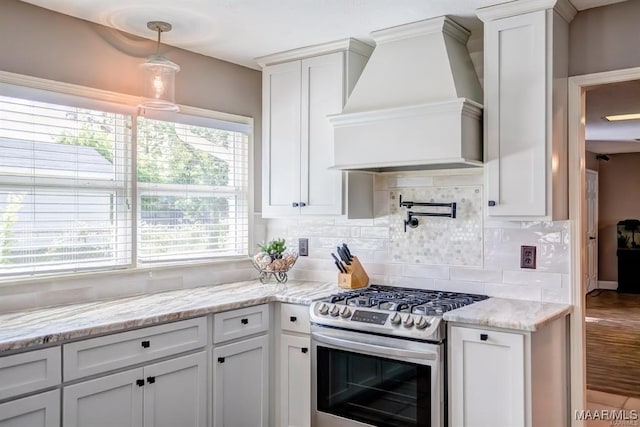 kitchen with pendant lighting, premium range hood, stainless steel range with gas stovetop, white cabinets, and decorative backsplash