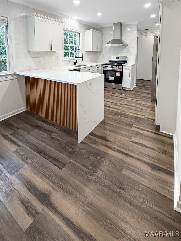 kitchen with wall chimney range hood, white cabinetry, stainless steel appliances, dark hardwood / wood-style flooring, and kitchen peninsula