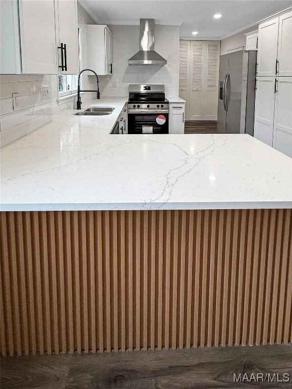 kitchen with appliances with stainless steel finishes, sink, white cabinets, light stone counters, and wall chimney exhaust hood