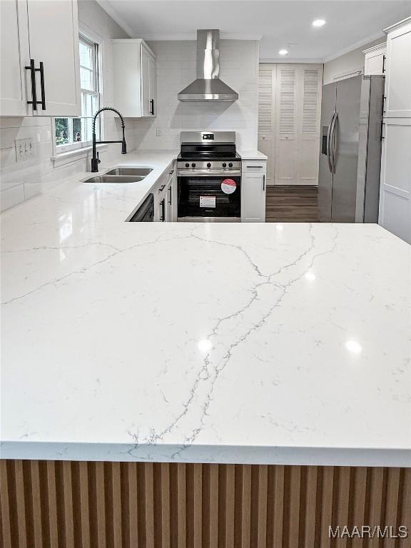 kitchen with wall chimney range hood, sink, appliances with stainless steel finishes, light stone counters, and white cabinets