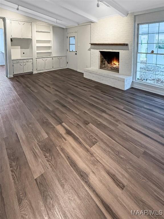 unfurnished living room featuring track lighting, a fireplace, beam ceiling, and dark hardwood / wood-style flooring