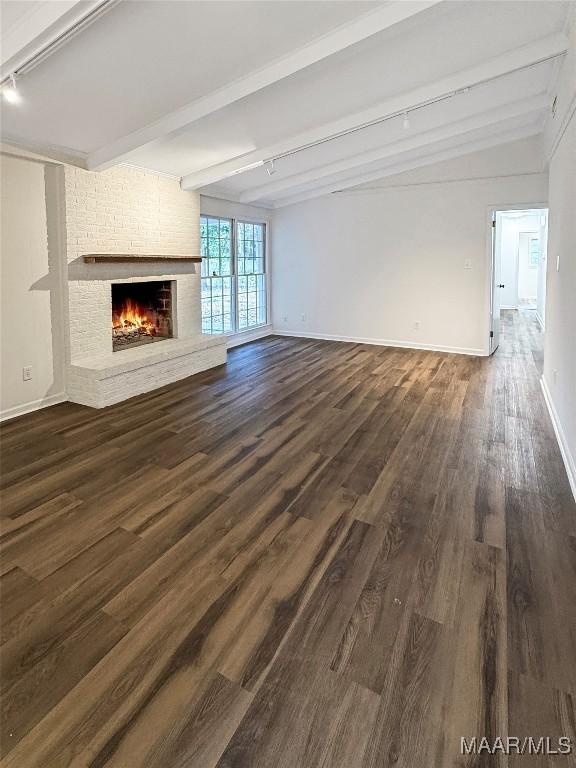 unfurnished living room with a brick fireplace, track lighting, vaulted ceiling with beams, and dark hardwood / wood-style floors