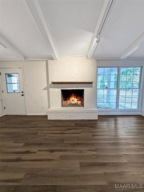 unfurnished living room with dark hardwood / wood-style floors, plenty of natural light, beam ceiling, and a brick fireplace