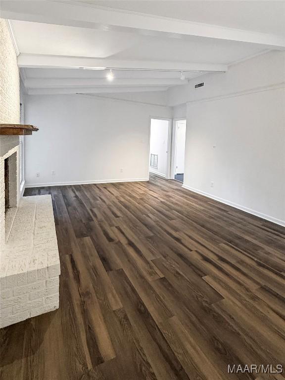 unfurnished living room featuring beamed ceiling, dark wood-type flooring, and a brick fireplace