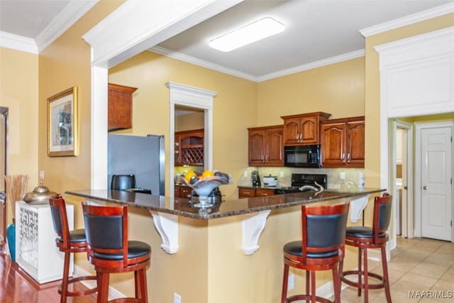 kitchen with a breakfast bar, ornamental molding, black appliances, decorative backsplash, and kitchen peninsula