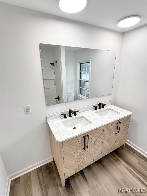 full bath with toilet, baseboards, a sink, and wood finished floors