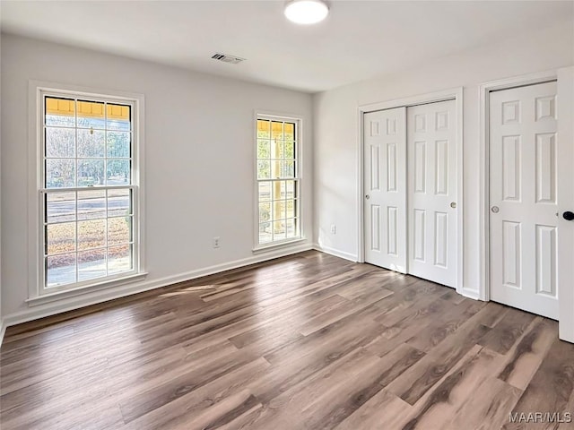 unfurnished bedroom with visible vents, baseboards, two closets, and dark wood-style floors