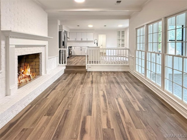 unfurnished living room featuring beamed ceiling, dark wood-type flooring, sink, and a fireplace