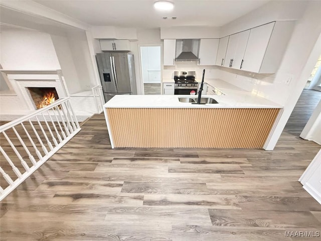 kitchen featuring hardwood / wood-style floors, white cabinetry, kitchen peninsula, stainless steel appliances, and wall chimney range hood