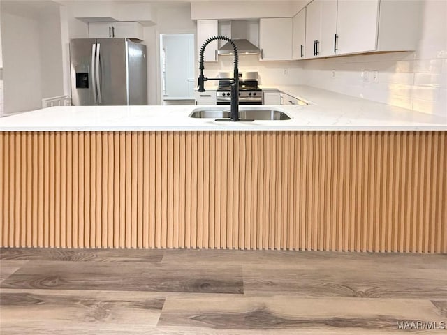 kitchen with tasteful backsplash, sink, white cabinets, stainless steel fridge with ice dispenser, and wall chimney range hood