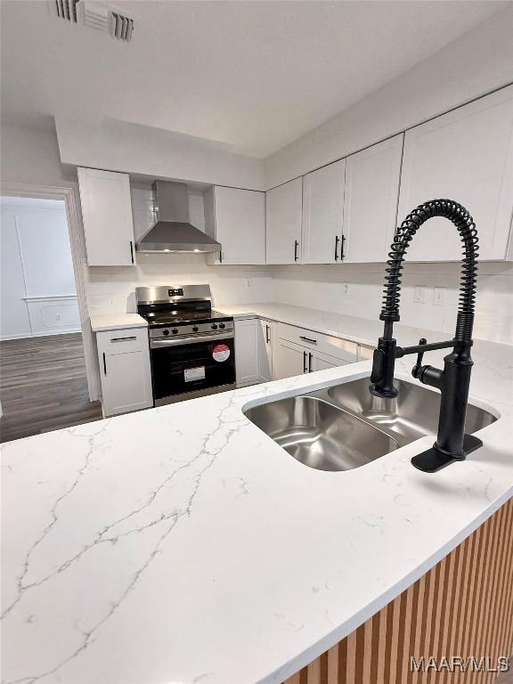 kitchen featuring sink, white cabinetry, wood-type flooring, stainless steel range, and wall chimney range hood