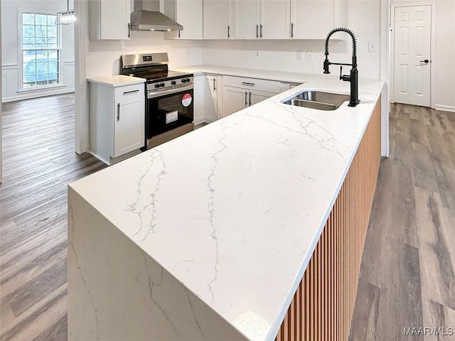 kitchen featuring stainless steel electric range, decorative light fixtures, sink, light wood-type flooring, and wall chimney exhaust hood