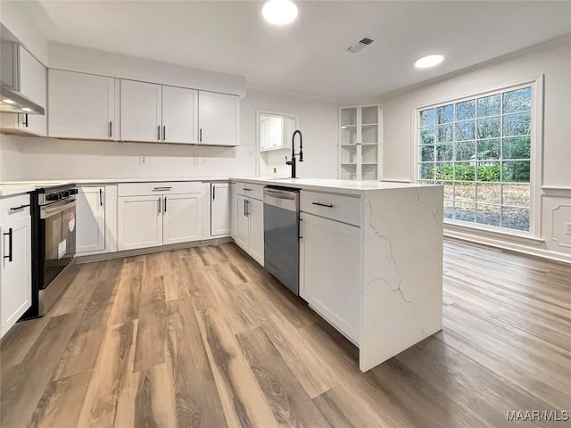 kitchen featuring kitchen peninsula, white cabinetry, light hardwood / wood-style floors, light stone counters, and stainless steel appliances