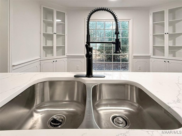 interior details featuring white cabinetry, sink, and light stone counters