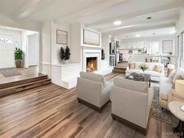 living area with a healthy amount of sunlight, a lit fireplace, light wood-type flooring, and beam ceiling