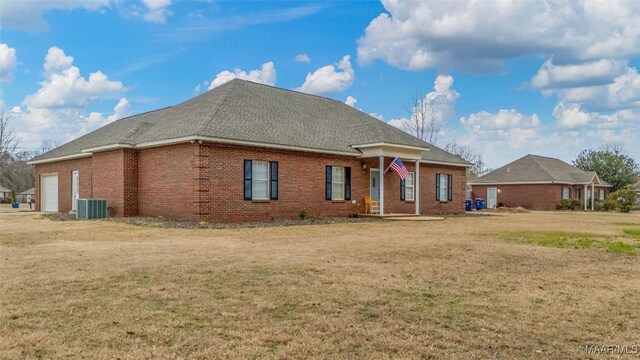 view of front of house with a front lawn, central AC unit, a garage, brick siding, and a shingled roof