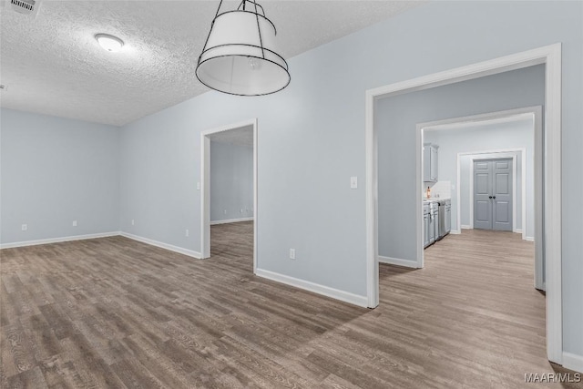 unfurnished dining area with wood finished floors, a textured ceiling, baseboards, and visible vents