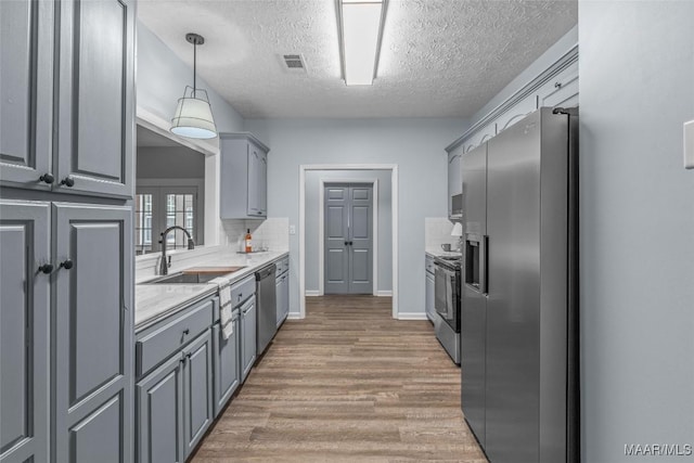 kitchen with a textured ceiling, a sink, light wood-type flooring, stainless steel appliances, and light countertops