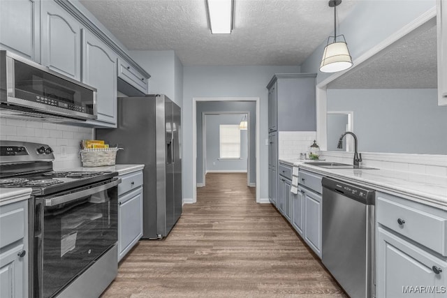 kitchen featuring stainless steel appliances, wood finished floors, gray cabinets, a sink, and a textured ceiling