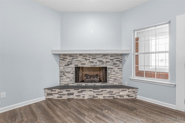 unfurnished living room with wood finished floors, a fireplace with raised hearth, and baseboards