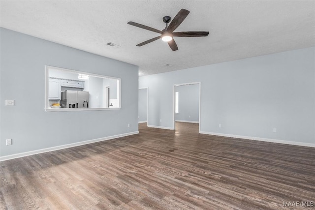 unfurnished living room featuring visible vents, a ceiling fan, baseboards, a textured ceiling, and dark wood-style flooring