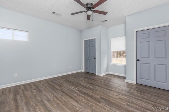 unfurnished bedroom with dark hardwood / wood-style flooring, ceiling fan, two closets, and a textured ceiling