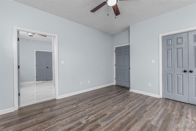 unfurnished bedroom featuring a textured ceiling, dark wood finished floors, baseboards, a closet, and ceiling fan