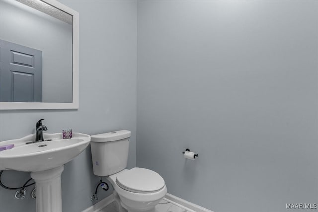 half bath with marble finish floor, toilet, baseboards, and a sink
