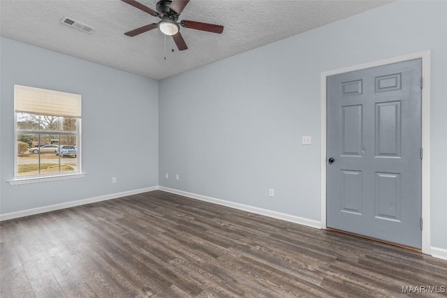 spare room with dark wood finished floors, visible vents, a ceiling fan, and baseboards