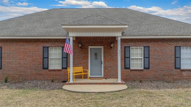 doorway to property featuring a shingled roof and brick siding