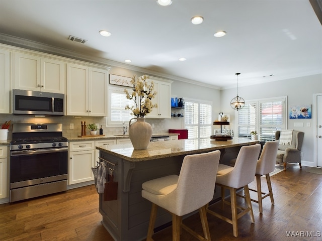 kitchen with pendant lighting, appliances with stainless steel finishes, a center island, and light stone countertops