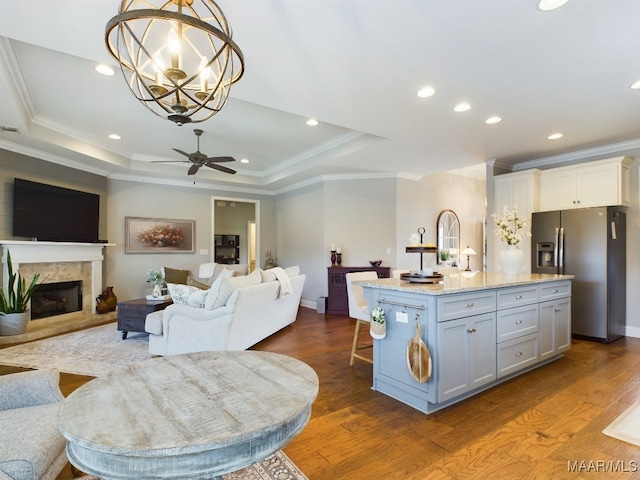 kitchen featuring stainless steel fridge with ice dispenser, hanging light fixtures, a raised ceiling, an island with sink, and white cabinets