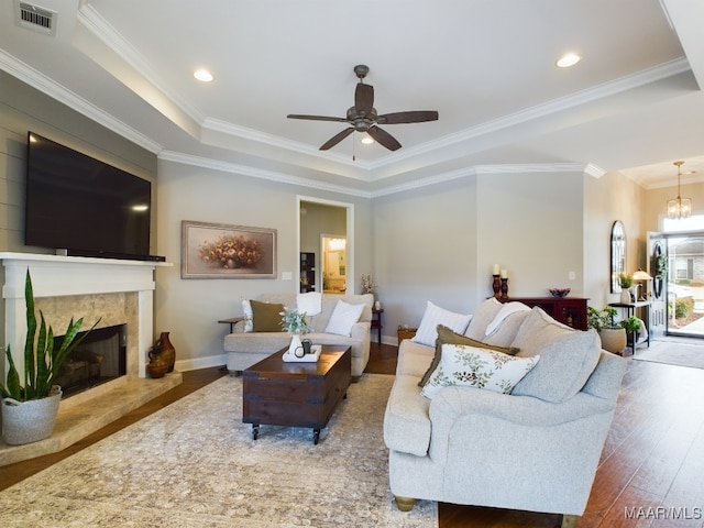 living room featuring ceiling fan with notable chandelier, wood-type flooring, ornamental molding, a high end fireplace, and a tray ceiling