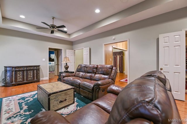 living room featuring hardwood / wood-style floors, ceiling fan, and a tray ceiling