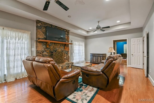 living room featuring a fireplace, a raised ceiling, ceiling fan, and light wood-type flooring