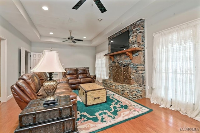 living room with light hardwood / wood-style flooring, a raised ceiling, and ceiling fan