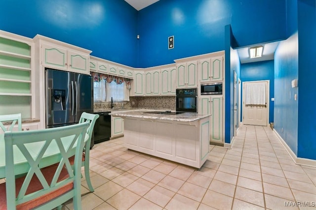 kitchen featuring light tile patterned floors, a center island, a high ceiling, black appliances, and light stone countertops