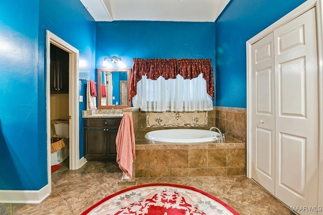 bathroom featuring a relaxing tiled tub, vanity, toilet, and tile patterned flooring