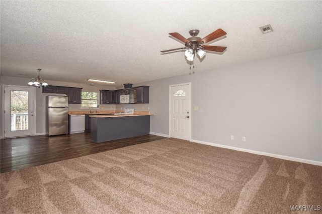 unfurnished living room with ceiling fan with notable chandelier, a textured ceiling, and dark carpet