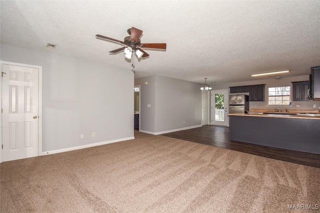 unfurnished living room featuring dark colored carpet, ceiling fan with notable chandelier, and a textured ceiling