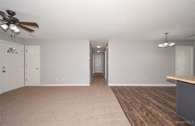 unfurnished living room featuring dark carpet, ceiling fan with notable chandelier, and a textured ceiling