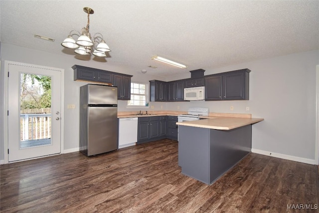 kitchen with pendant lighting, white appliances, dark wood-type flooring, and kitchen peninsula