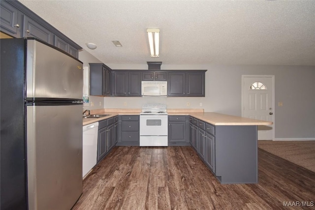 kitchen with sink, dark hardwood / wood-style floors, gray cabinets, kitchen peninsula, and white appliances