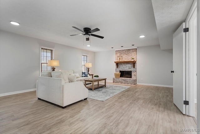 living room with ceiling fan, a fireplace, and light wood-type flooring