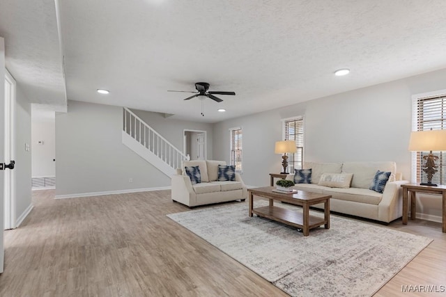 living room featuring ceiling fan, a textured ceiling, and light wood-type flooring