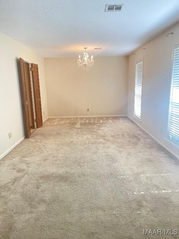 unfurnished room with light colored carpet, a textured ceiling, and a chandelier