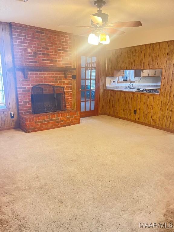 unfurnished living room with light carpet, a fireplace, ceiling fan, and wood walls