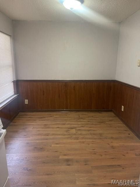 unfurnished room featuring wood-type flooring, wooden walls, and a textured ceiling